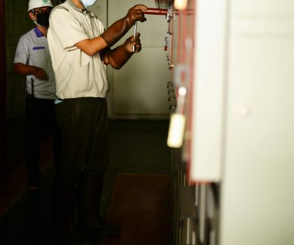 Two electricians working on control panels in an industrial indoor setting.