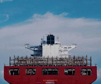 Large red cargo ship transporting goods across the ocean under a bright blue sky.